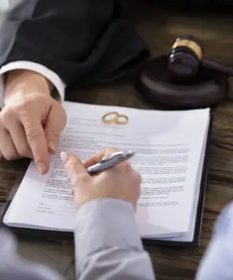 The lawyer is pointing with his finger for the groom to sign the marriage papers during a court marriage in Karachi, with two marriage rings lying beside a gavel on the table.